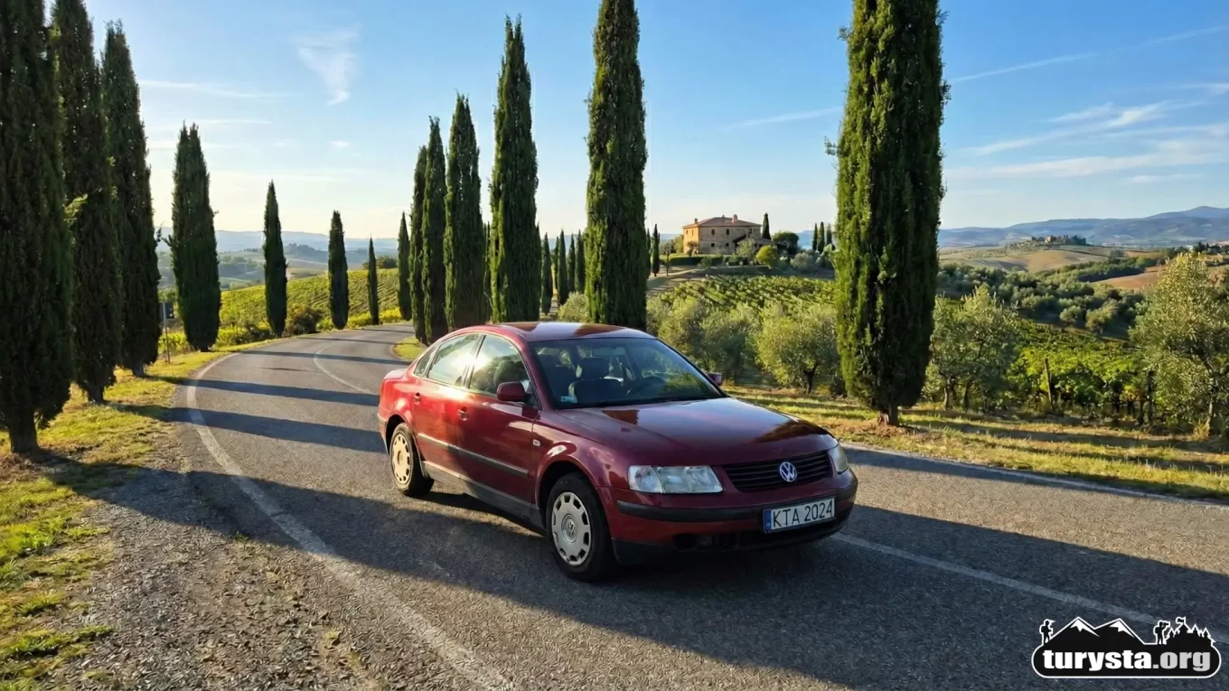 Czerwony samochód na malowniczej drodze w Toskanii - poradnik o wyjeździe do Włoch, przepisach drogowych i wyposażeniu.