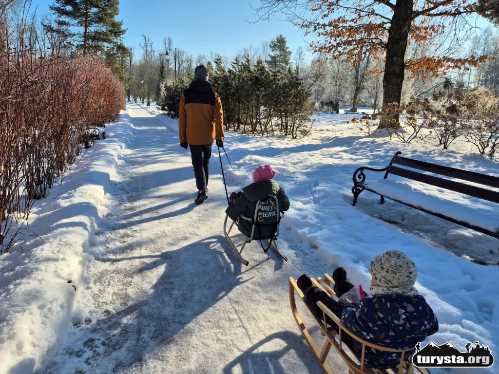 Zimowy spacer z dzieckiem na sankach szeroką alejką w Parku Zdrojowym w Rabce-Zdroju.