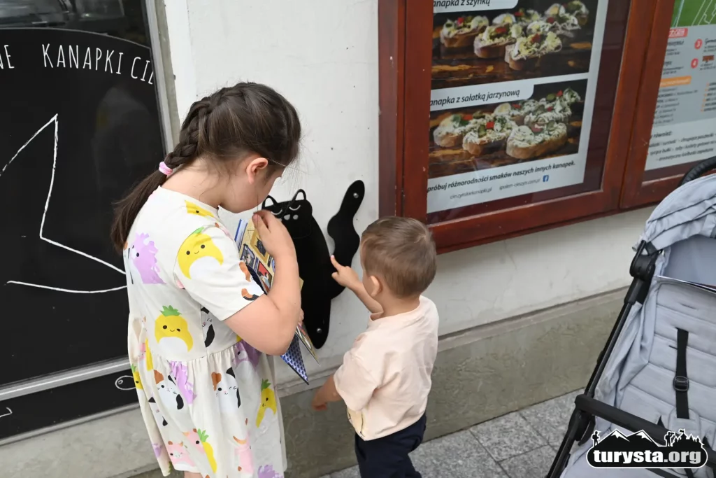 Dwoje dzieci szukające ukrytych figurek kotów na ulicy w Cieszynie.
