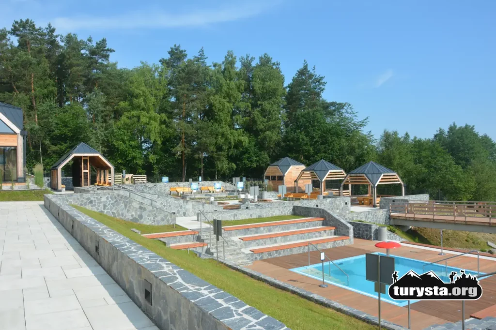 Nowoczesny Park Zdrojowy w Ciężkowicach z zewnętrznymi basenami do hydroterapii, zadbanymi ścieżkami i drewnianymi wiatami.