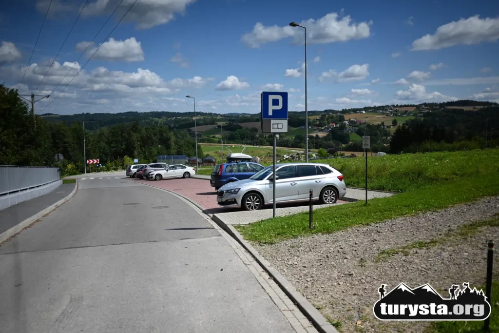 Darmowy parking górny przy ulicy Spokojnej obok Parku Zdrojowego w Ciężkowicach z widokiem na zaparkowane samochody i wzgórza.
