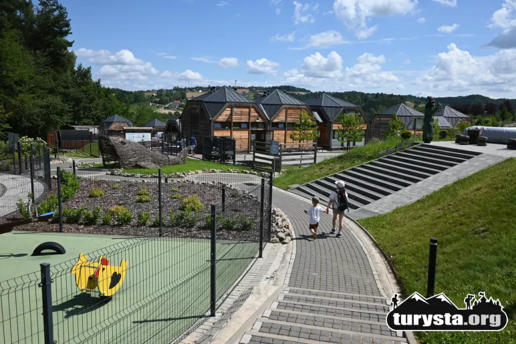 Dzieci idące brukowaną alejką obok placu zabaw i nowoczesnych drewnianych domków w Parku Zdrojowym w Ciężkowicach.