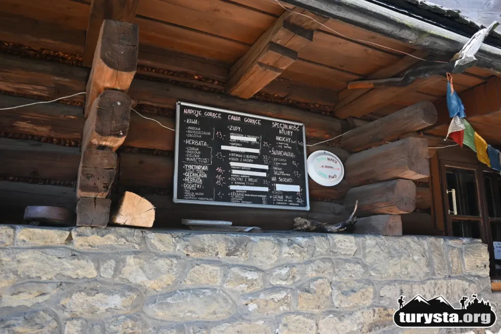 Tablica z menu i cennikiem dań przy drewnianym schronisku na Łapsowej Polanie