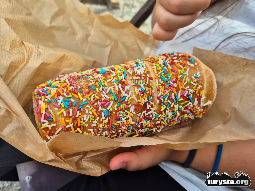 Ciepły trdelnik z kolorową cukrową posypką trzymany przez dziecko