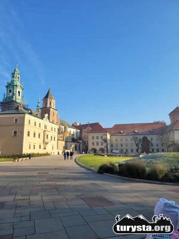 Przestronny dziedziniec zewnętrzny Zamku Królewskiego na Wawelu w słoneczny dzień. W tle widoczna charakterystyczna wieża.